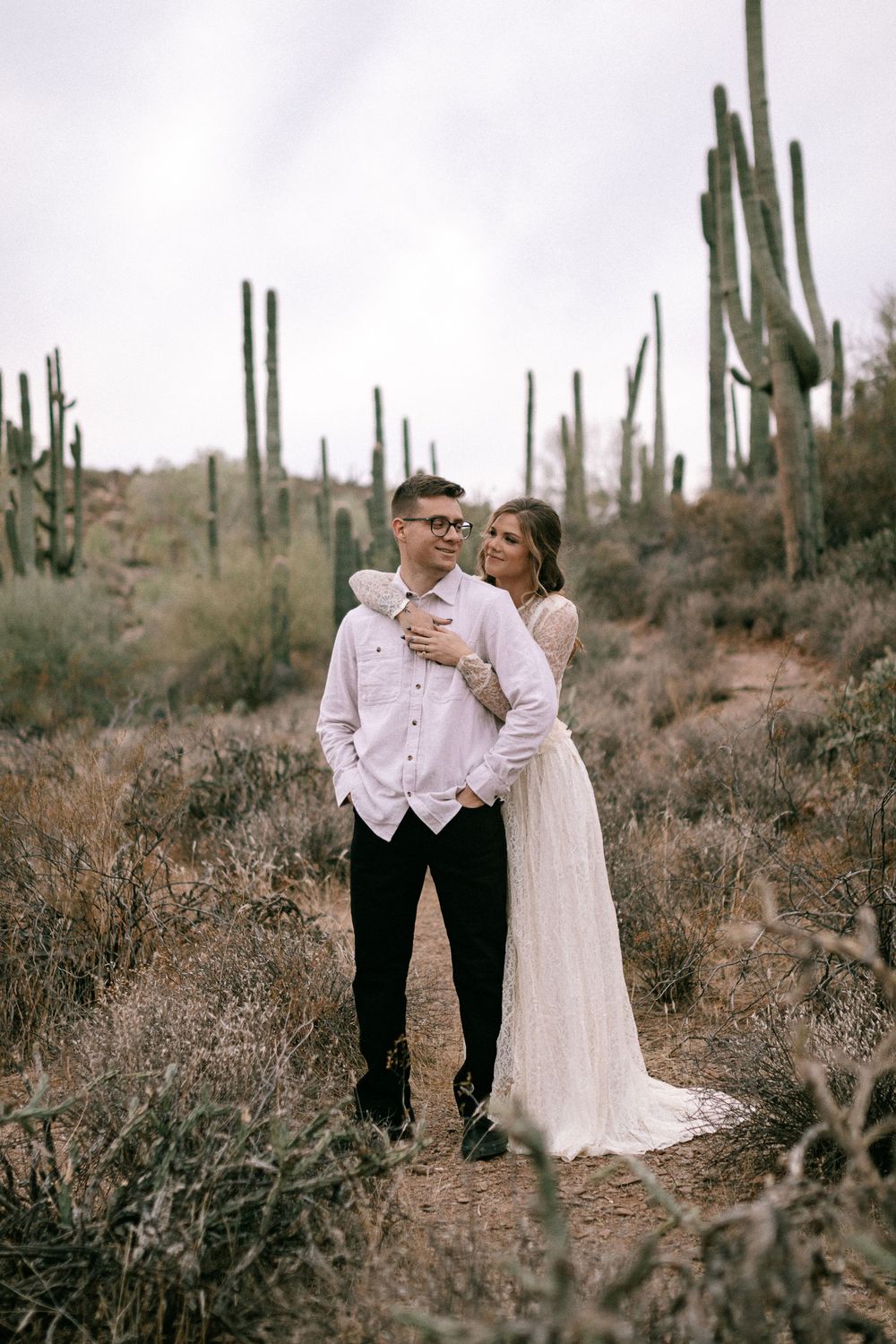 Romantic desert engagement photo with towering saguaro cacti creating a dramatic backdrop.