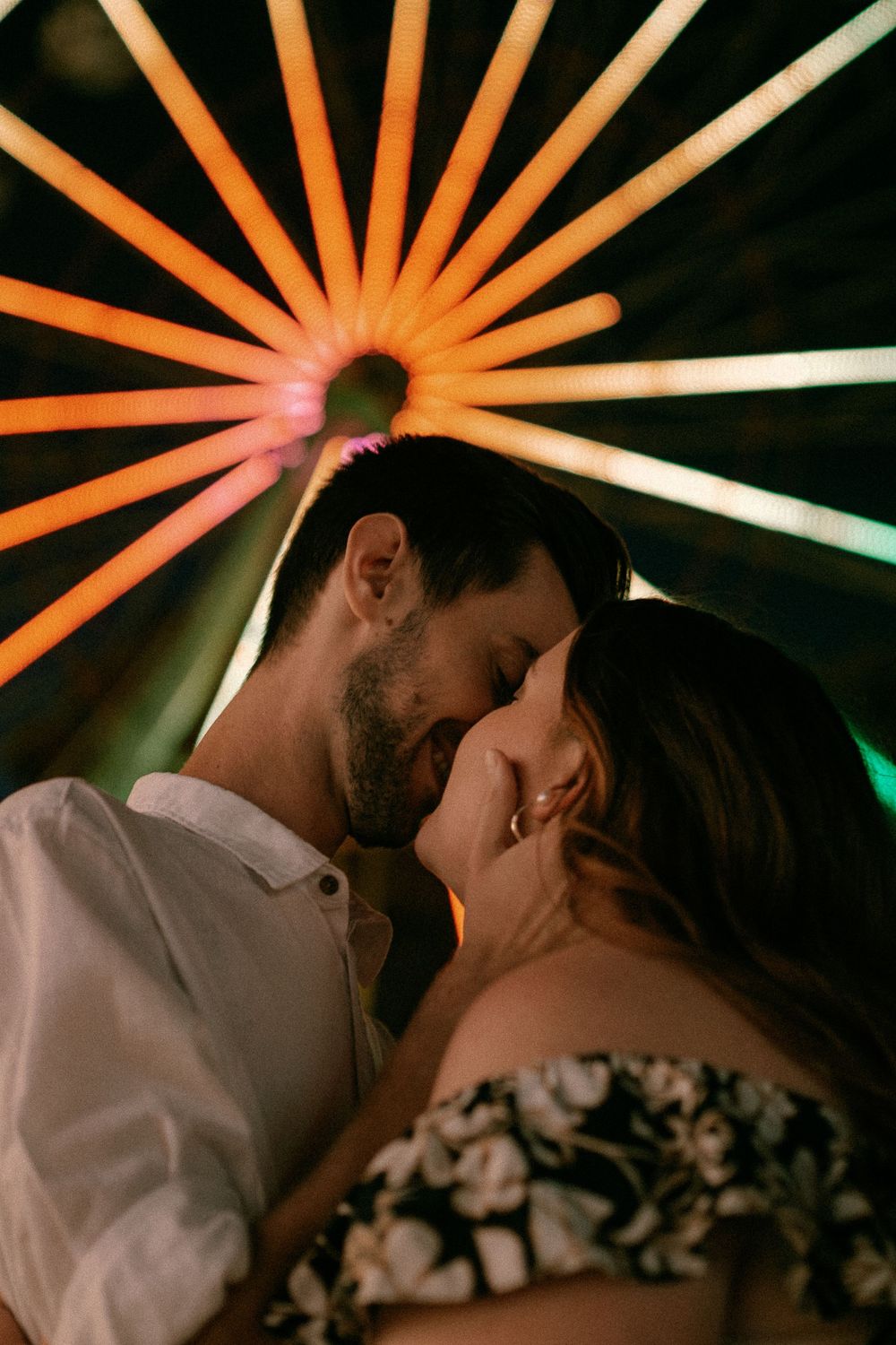 Romantic couple sharing a moment under colorful sunburst lighting at night.