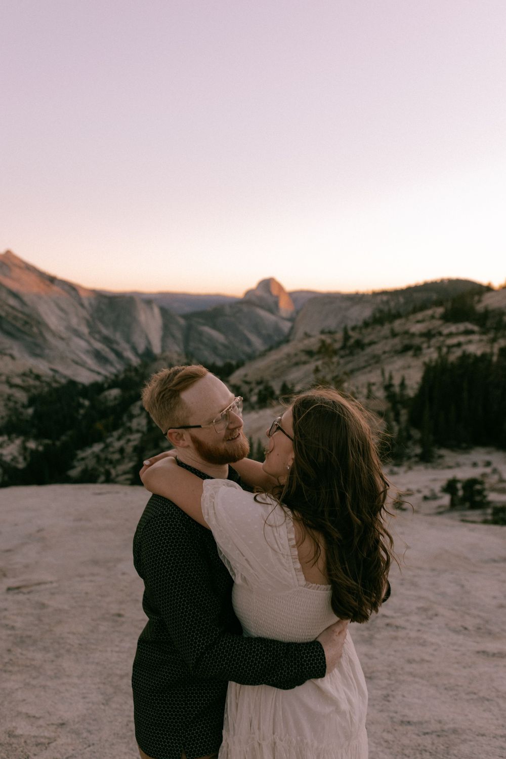 Couple embraces against scenic mountain backdrop during sunset in desert landscape.