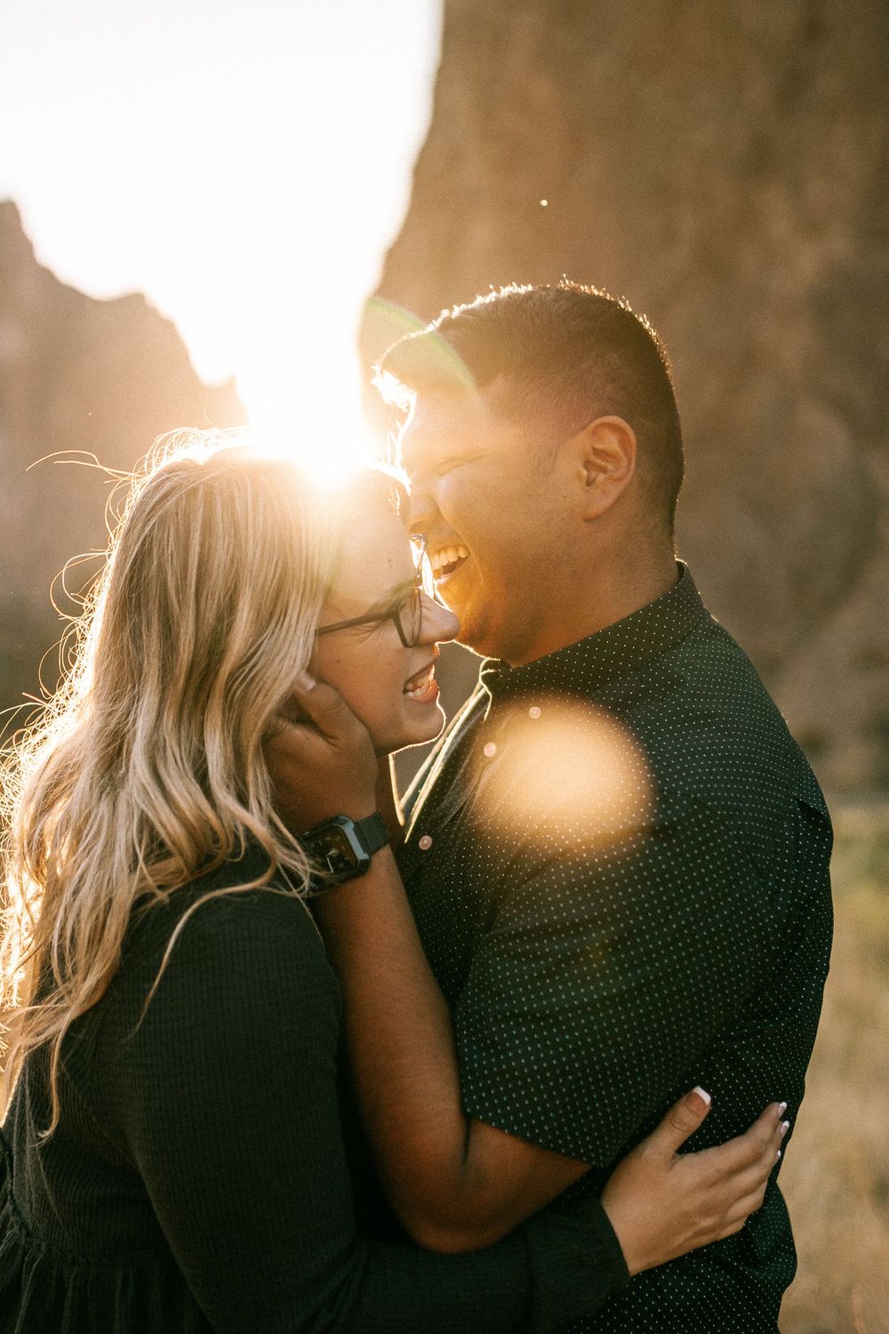 Couple sharing an intimate laugh during golden hour against rocky cliffs.