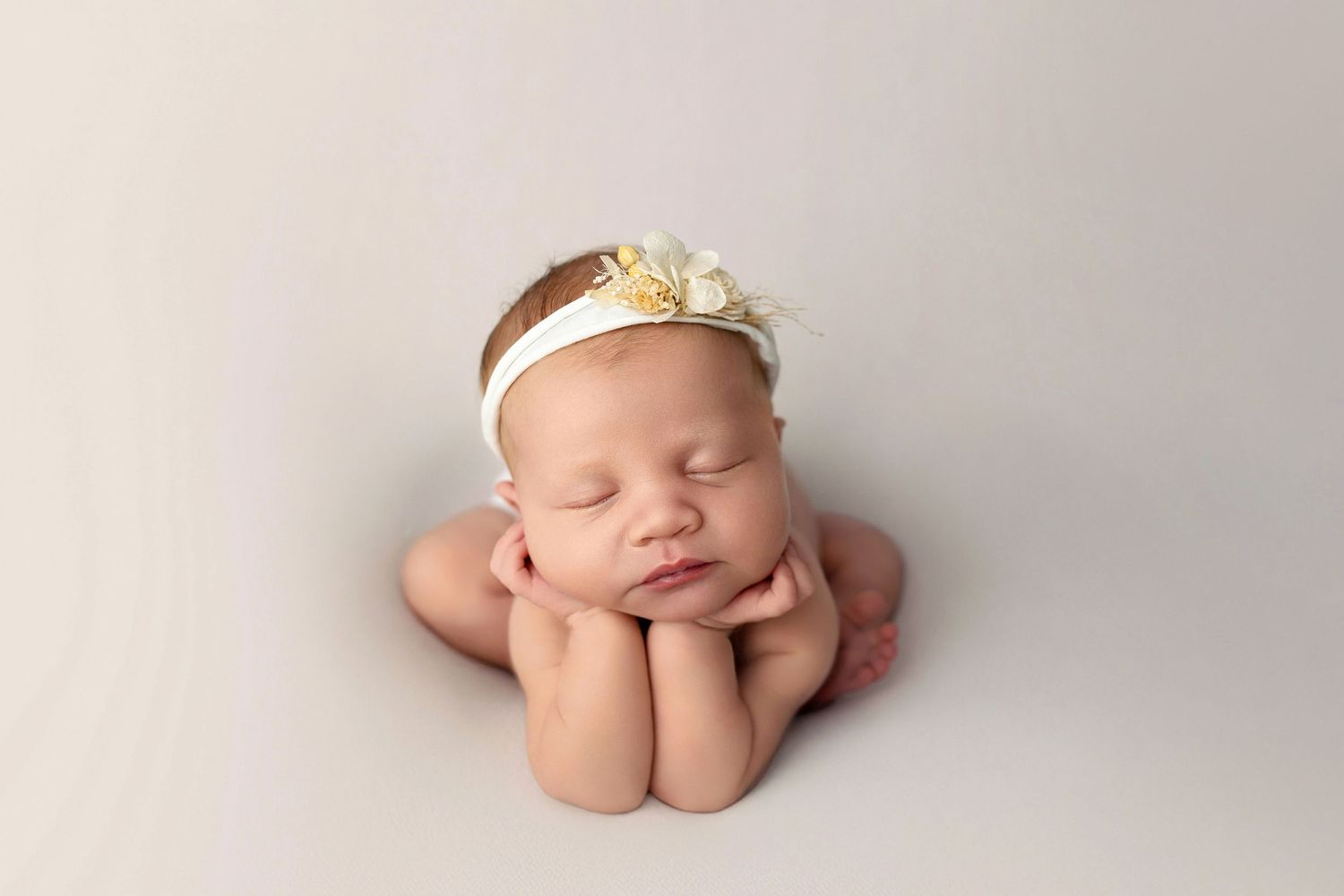 Sleeping newborn baby wearing soft gray knit sweater curled up on cream colored blanket in gentle studio lighting.