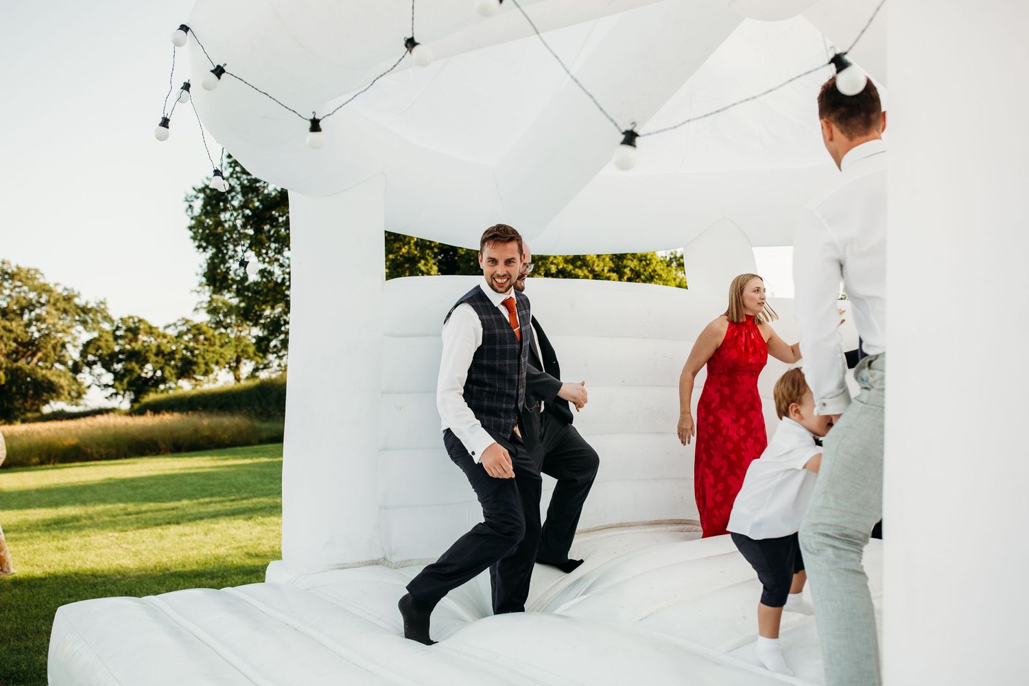 Wedding guests enjoying themselves on a white bouncy castle at an outdoor reception.