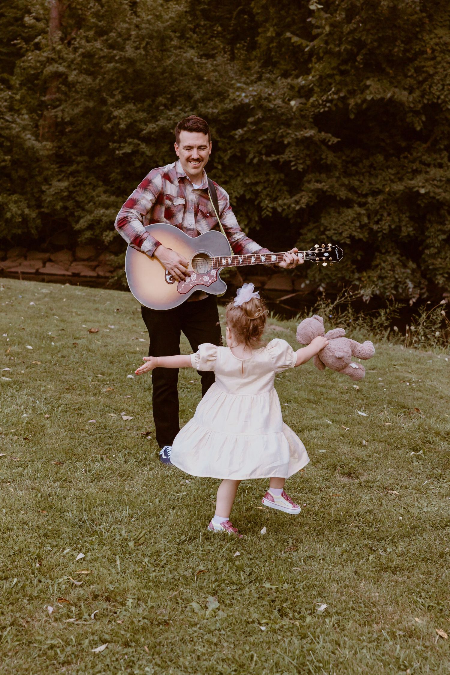 Sweet moment of dancing and guitar playing in a grassy outdoor setting.