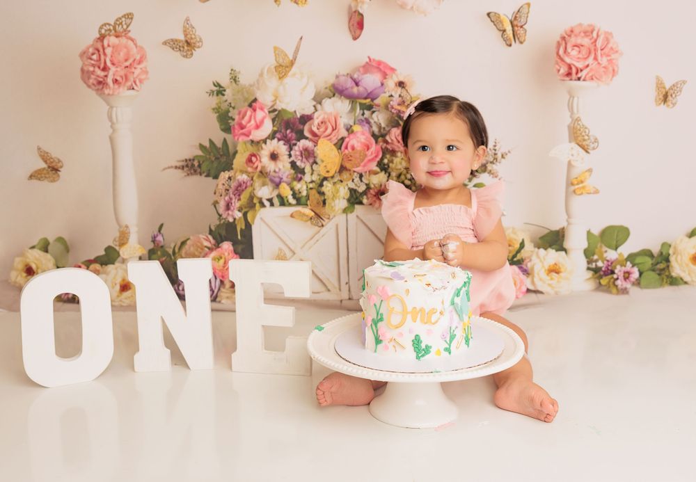 Pink and floral themed first birthday portrait with decorative cake.