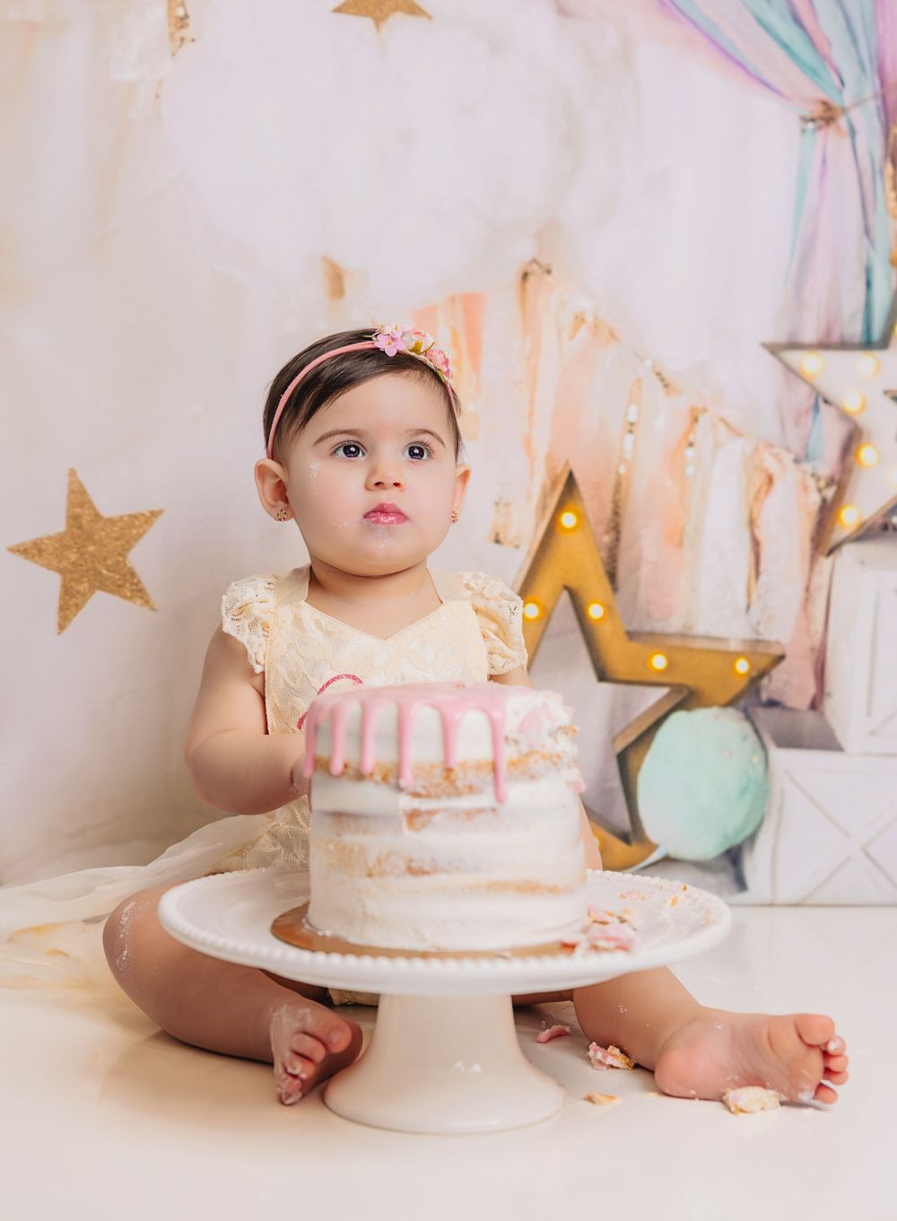 Baby sitting with birthday cake on white stand against starry backdrop.