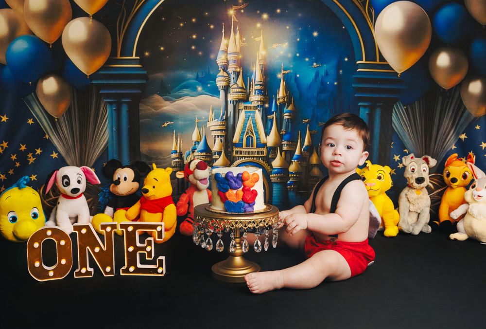 Disney-themed first birthday setup with castle backdrop, plush characters, and gold 'ONE' marquee letters.