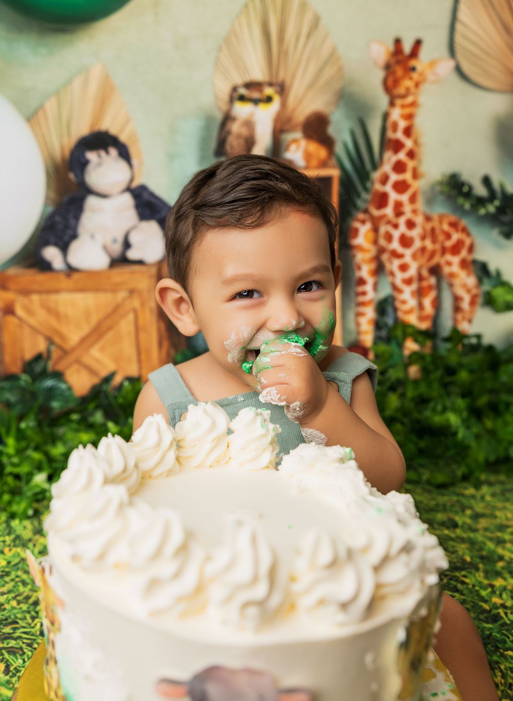 White birthday cake with safari decorations and balloon arch in the background.