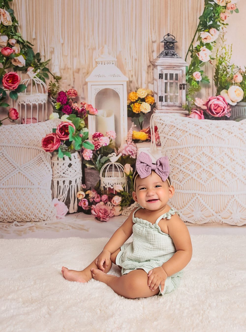 Baby in mint romper sitting on floor with floral backdrop featuring pink roses and white lanterns.