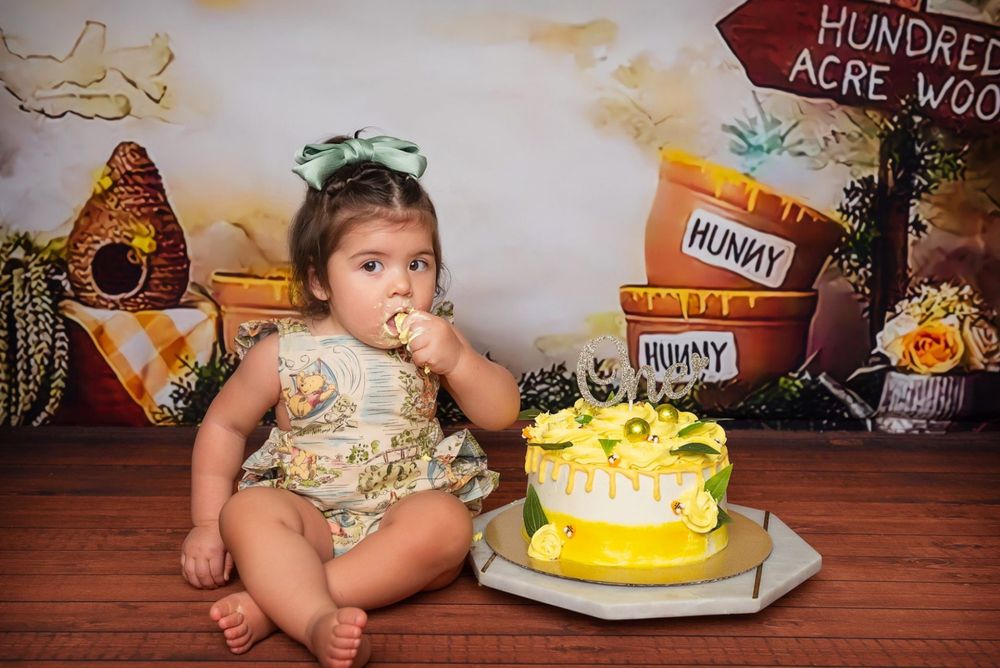 Baby in vintage Winnie the Pooh themed setting with yellow birthday cake.