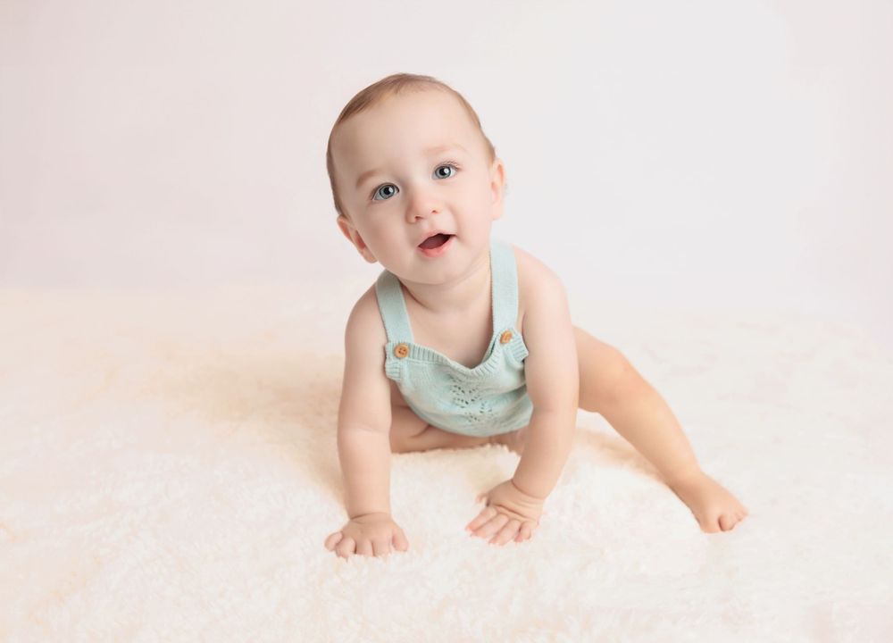 Baby in mint green romper crawling on light background in studio setting.