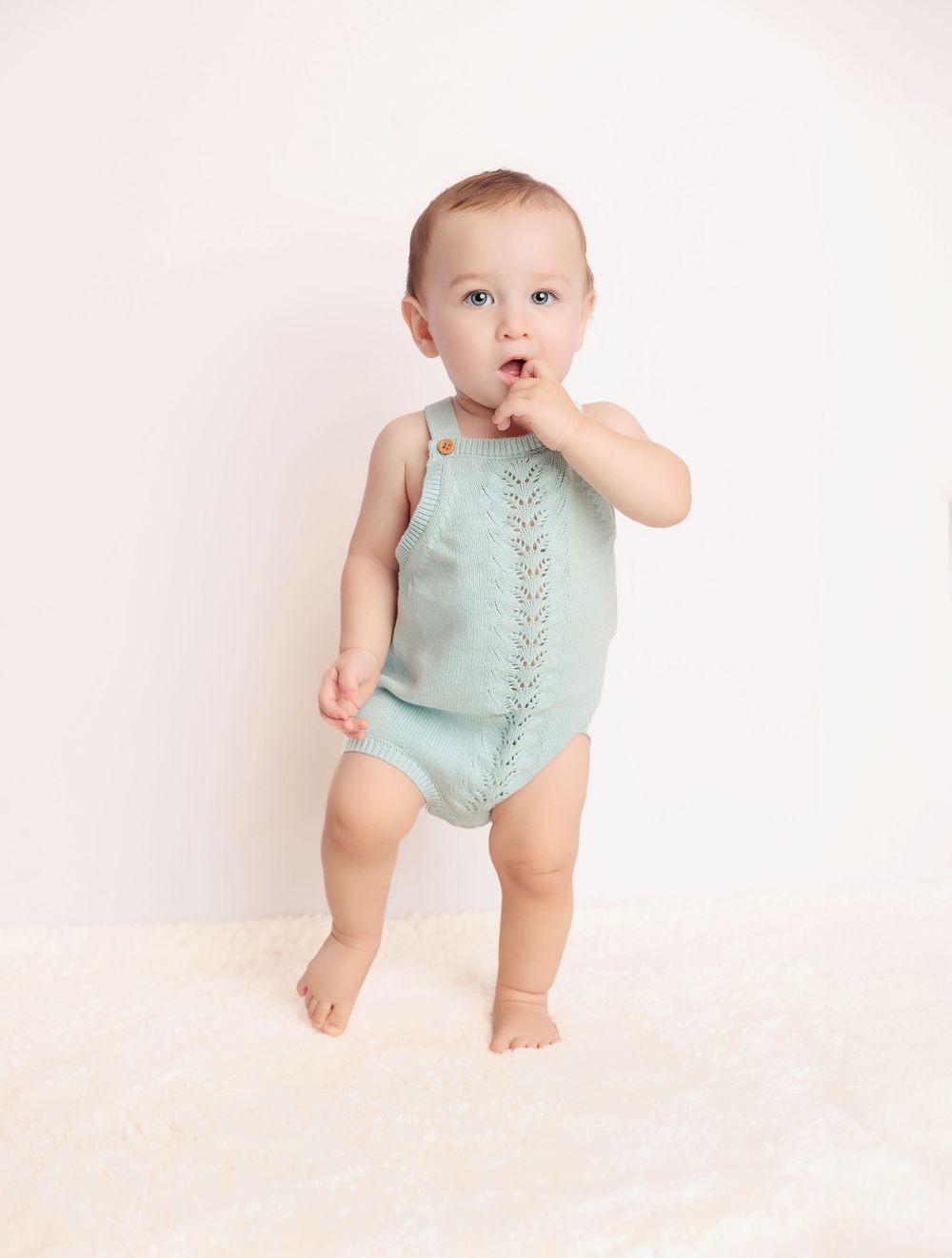 Baby wearing mint green outfit standing against soft pink background.