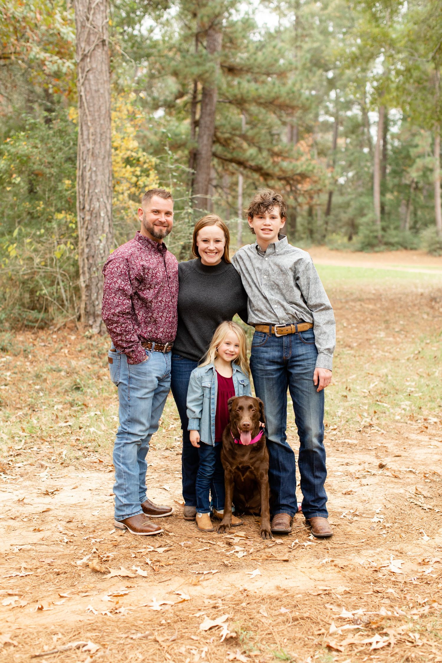 A family portrait with their chocolate lab dog on a forest trail in autumn.