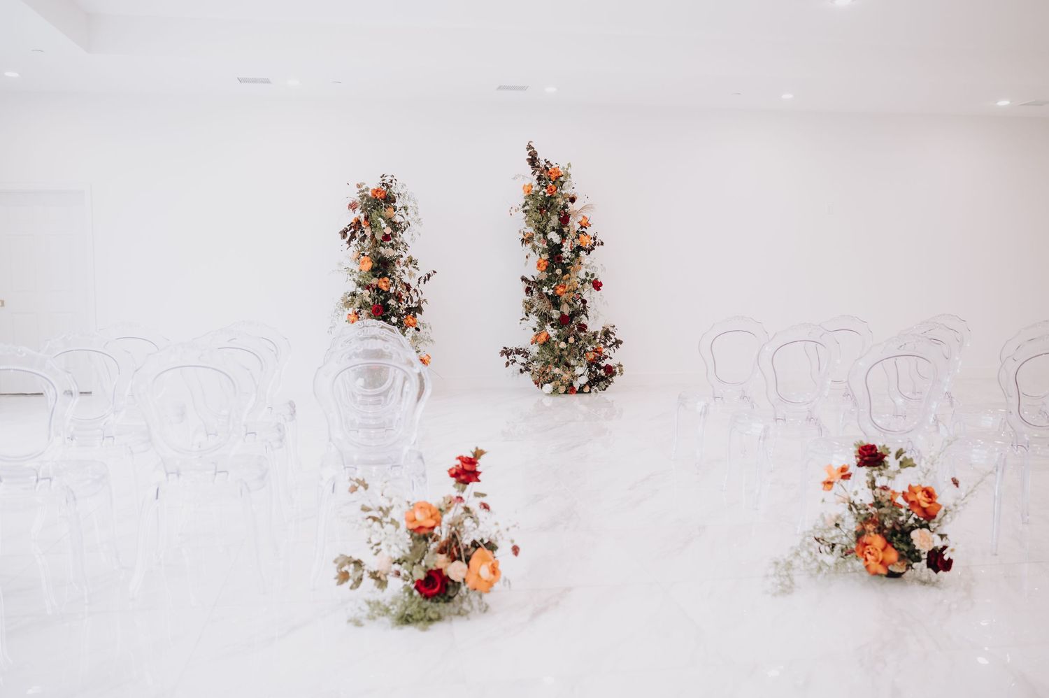 Wedding floral arrangements with orange and white flowers displayed on white marble floor.