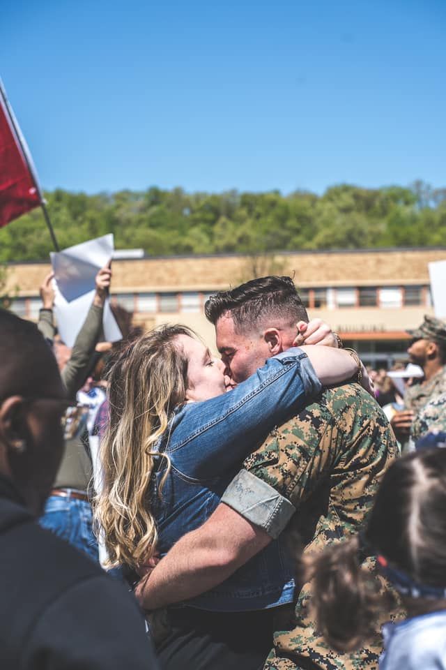 marine and girlfriend kiss in a crowd during a homecoming