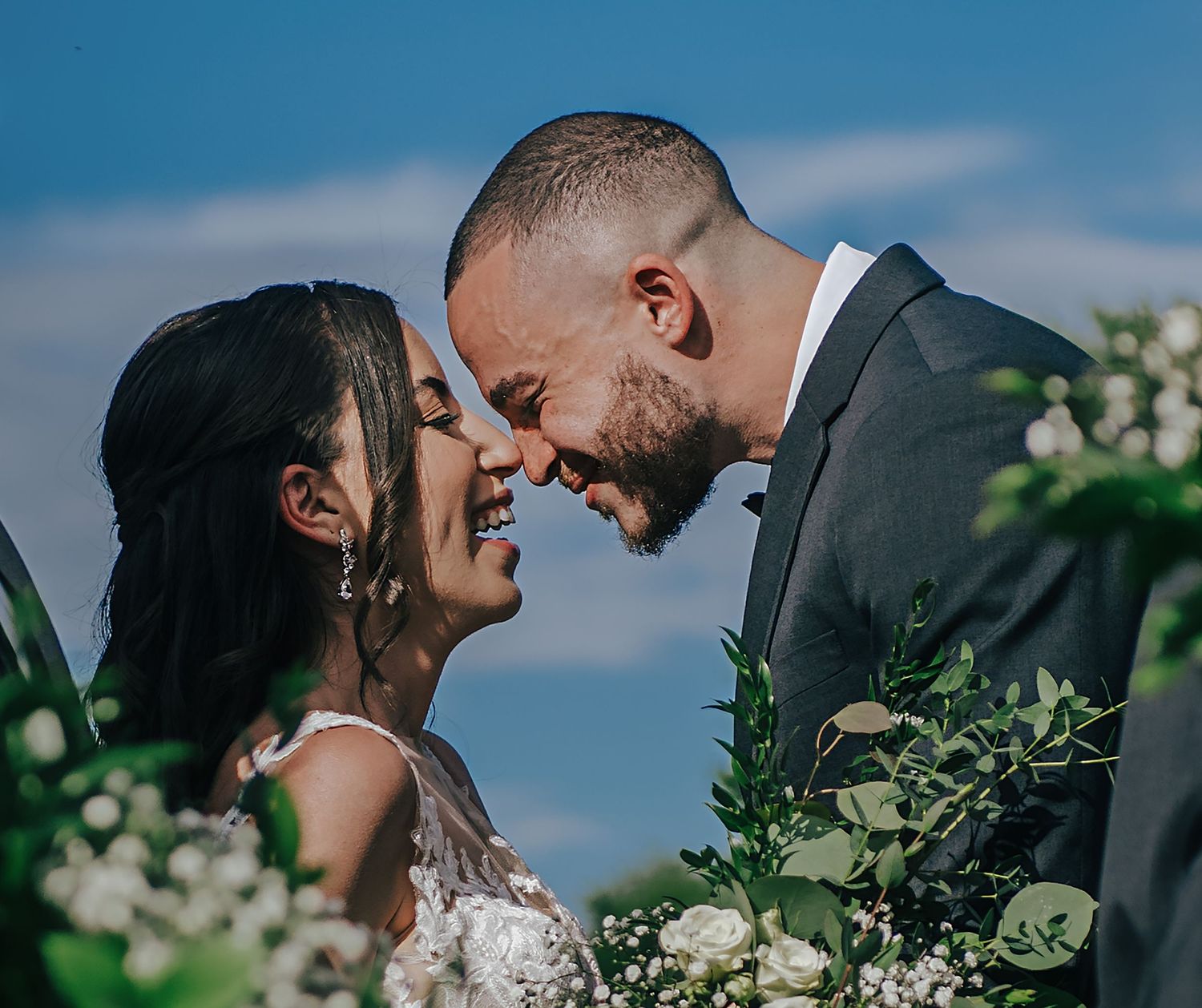 Intimate wedding portrait against blue sky with natural greenery.