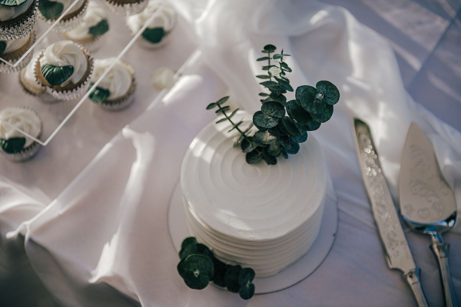 White wedding cupcakes and desserts arranged on elegant serving plates.