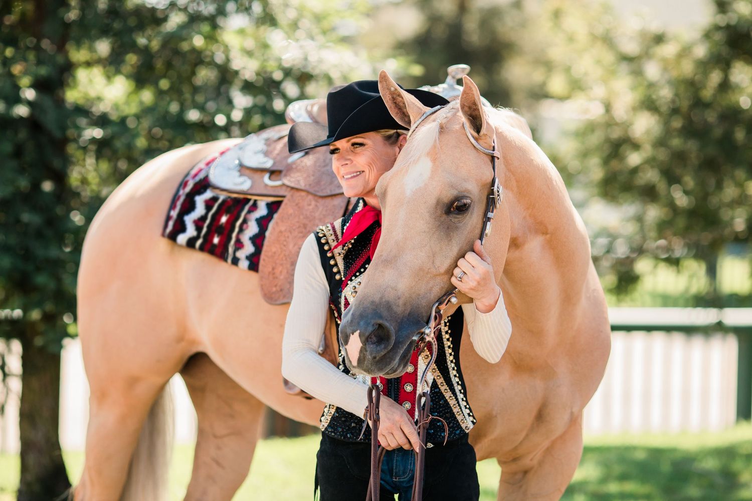 Horse and rider share tender moment with pale colored horse wearing decorative saddle.