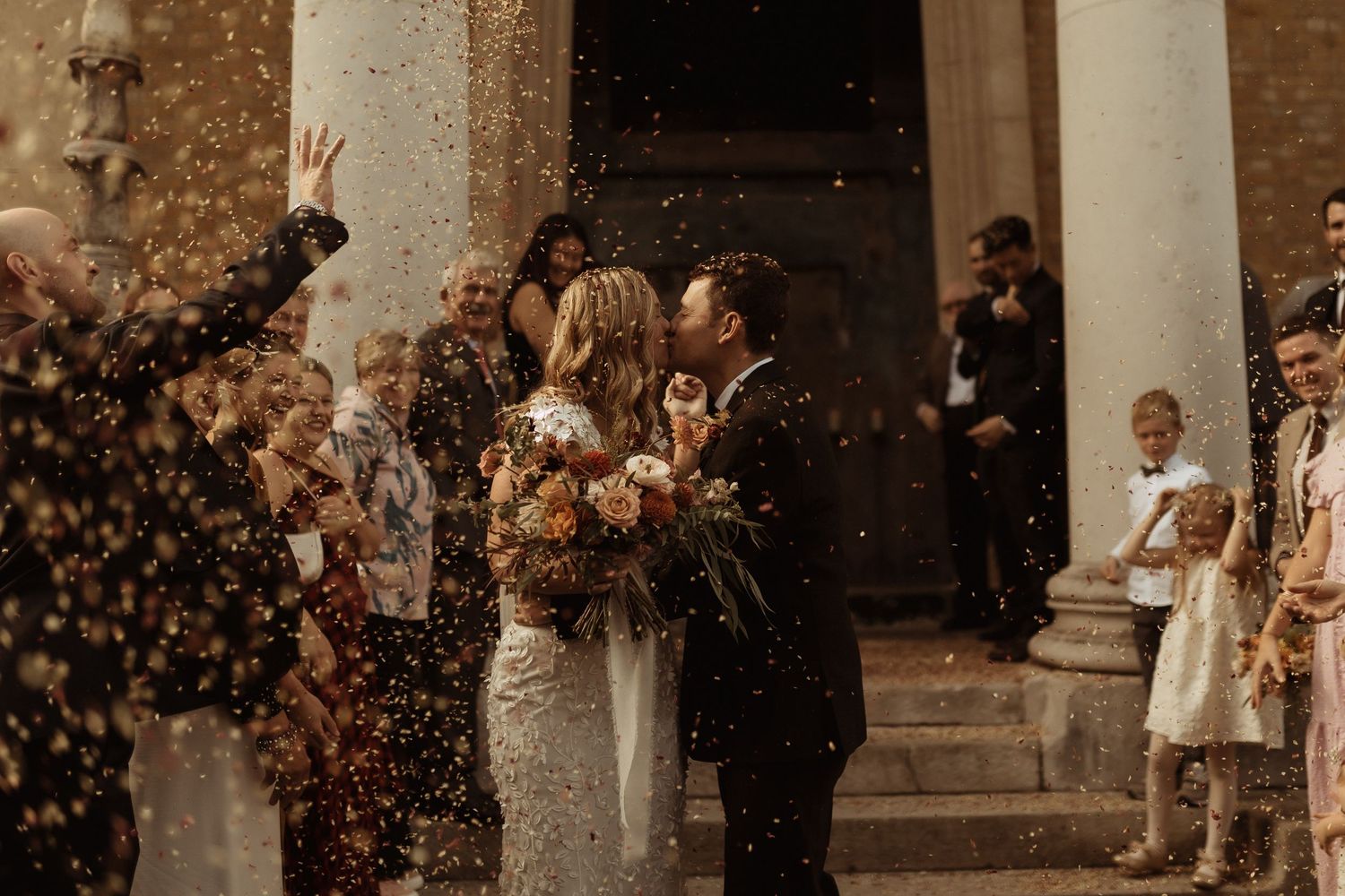 A joyful wedding celebration with confetti being thrown outside a columned building.
