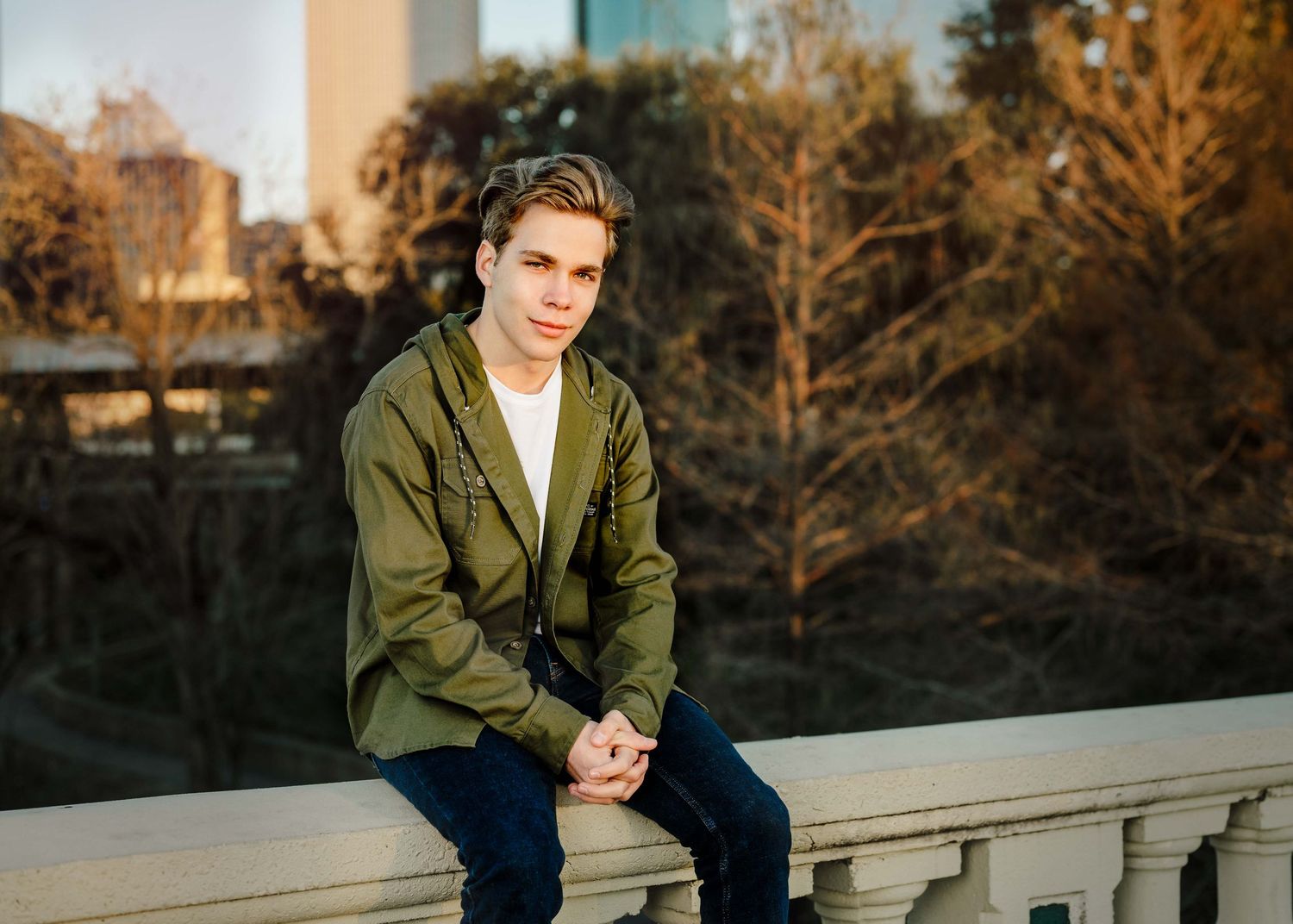 Outdoor portrait session at sunset with person in olive jacket against urban backdrop.