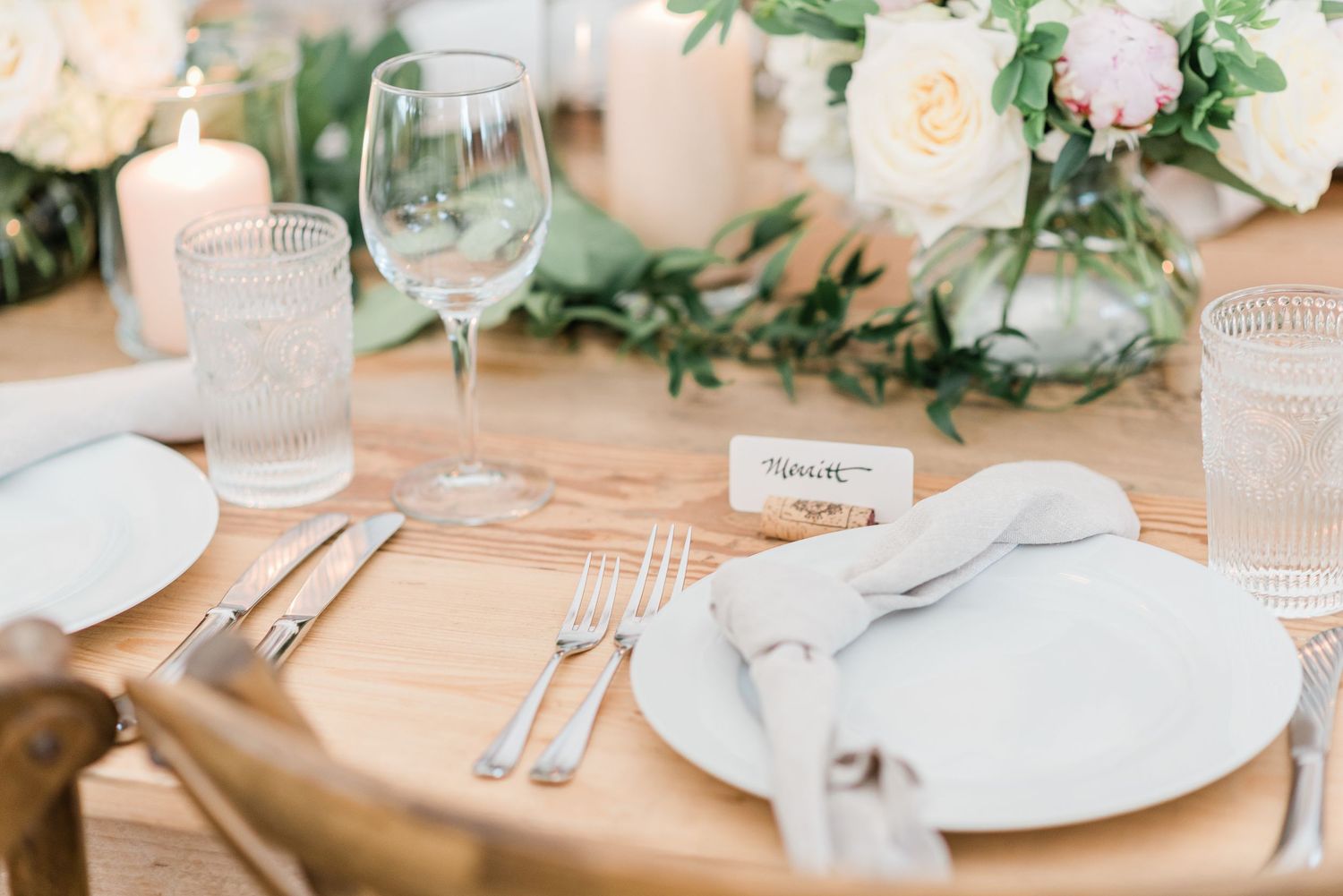 Table setting featuring greenery, candles, and wine cork nametags