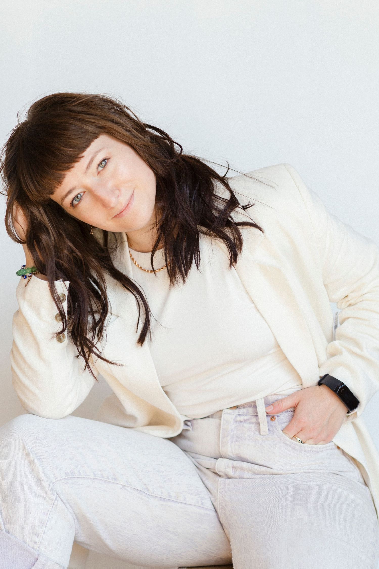 A casual portrait against a white background featuring cream-colored clothing and relaxed styling.