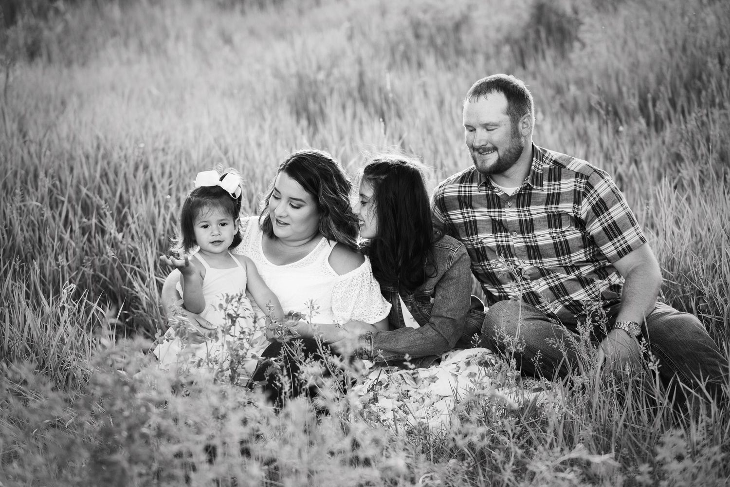 A black and white portrait of a family sitting together in a wildflower meadow on a sunny day.