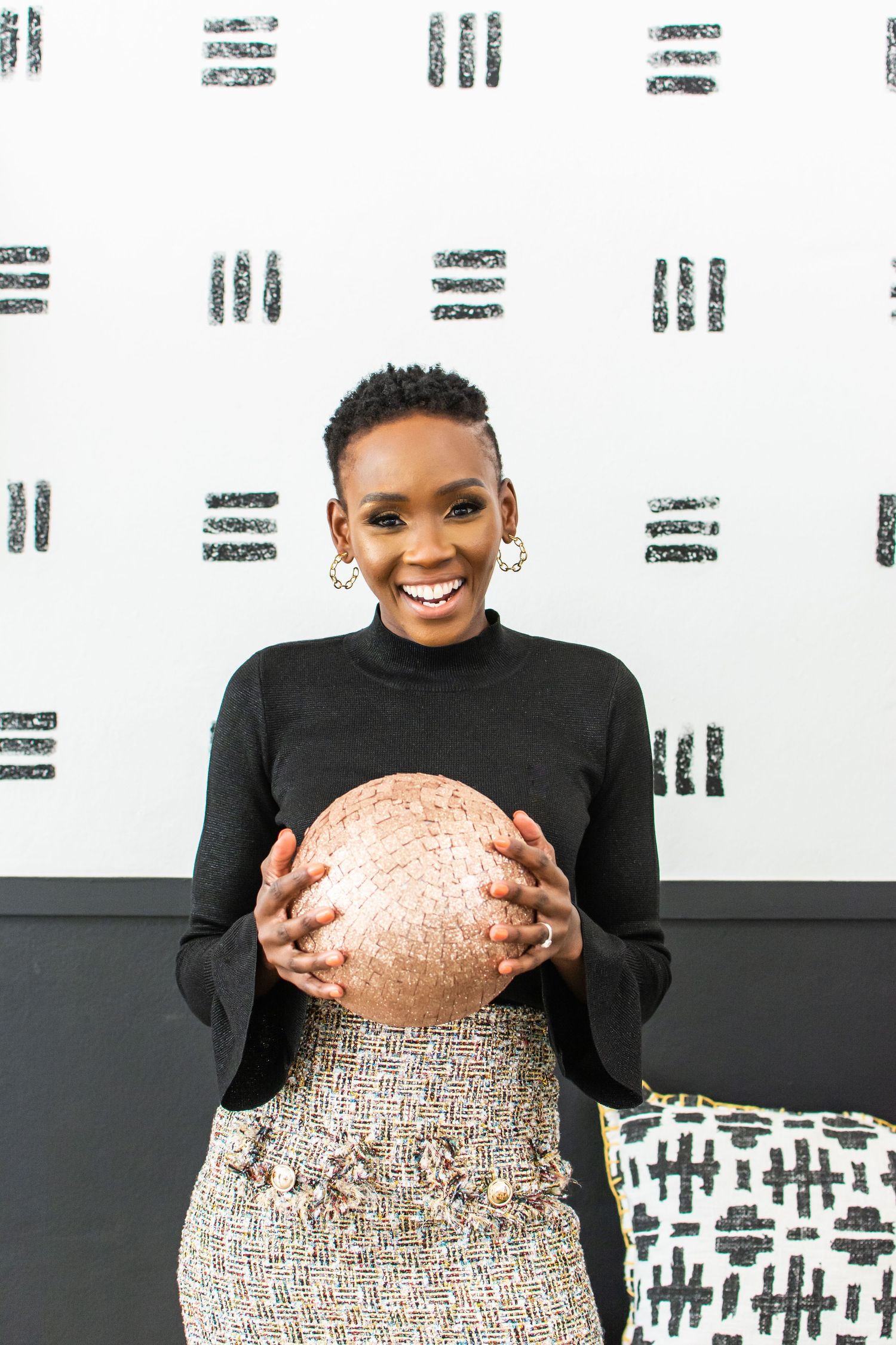 Fashion photo with black turtleneck and tweed skirt holding a large copper metallic sphere.