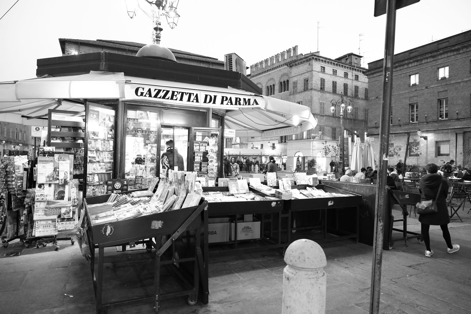 Black and white image of Gazzetta di Parma newsstand displaying magazines and newspapers in Italy.