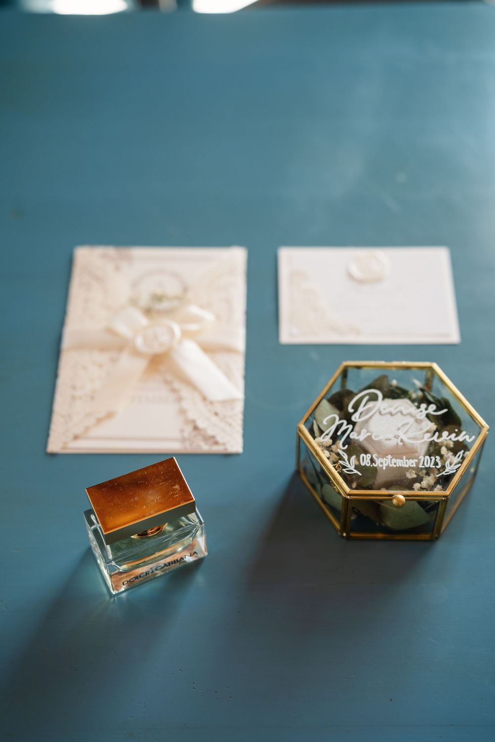 Elegant wedding invitations with wax seals and decorative glass boxes on teal surface.
