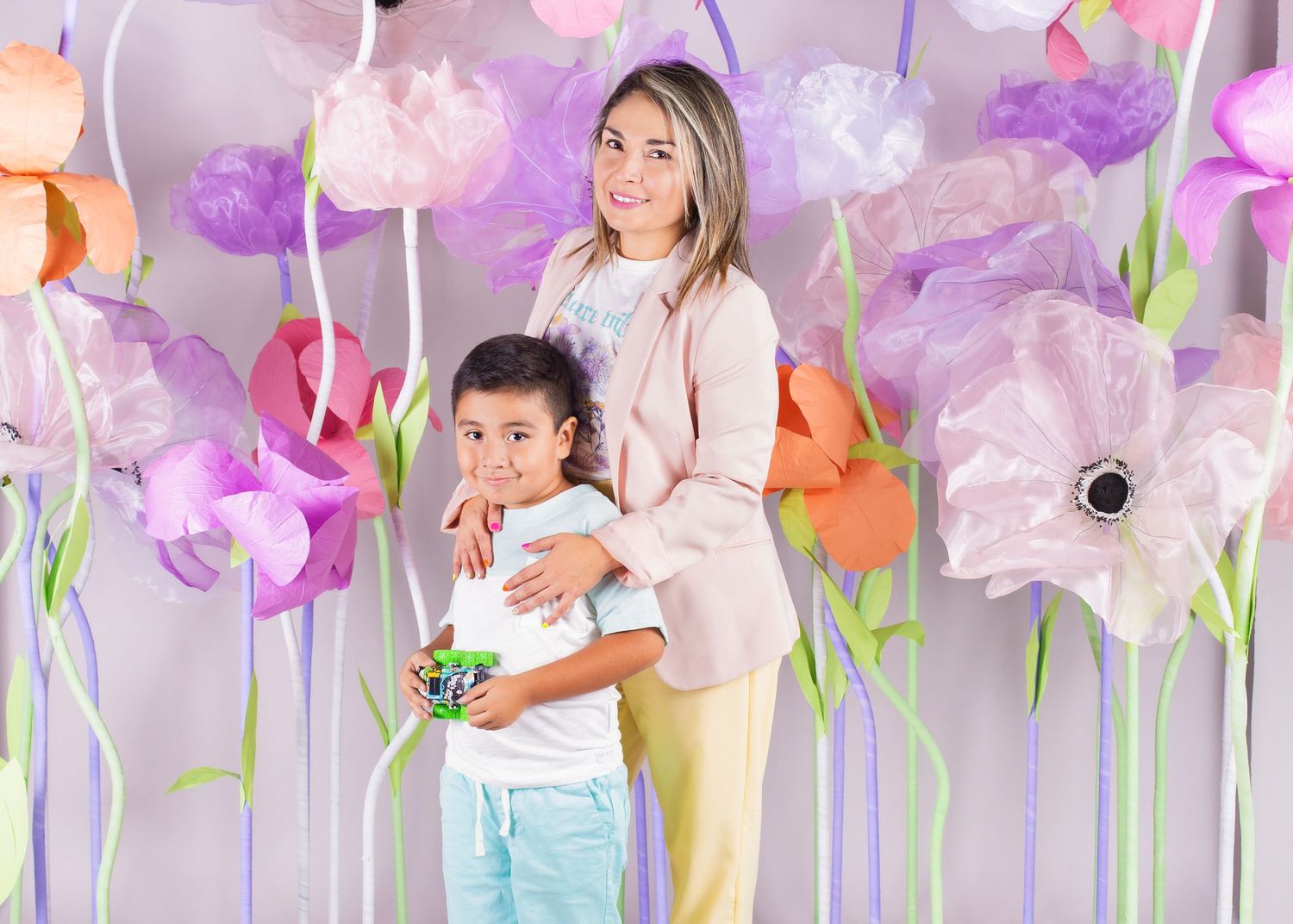 A woman and young boy pose together in front of a colorful backdrop of large decorative paper flowers.
