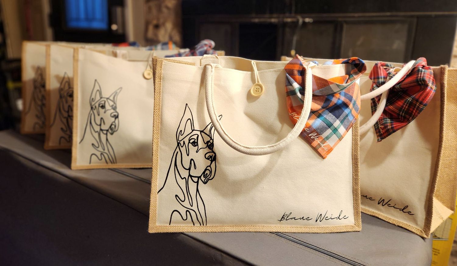 A row of tote bags featuring Great Dane illustrations displayed on a table at an event.