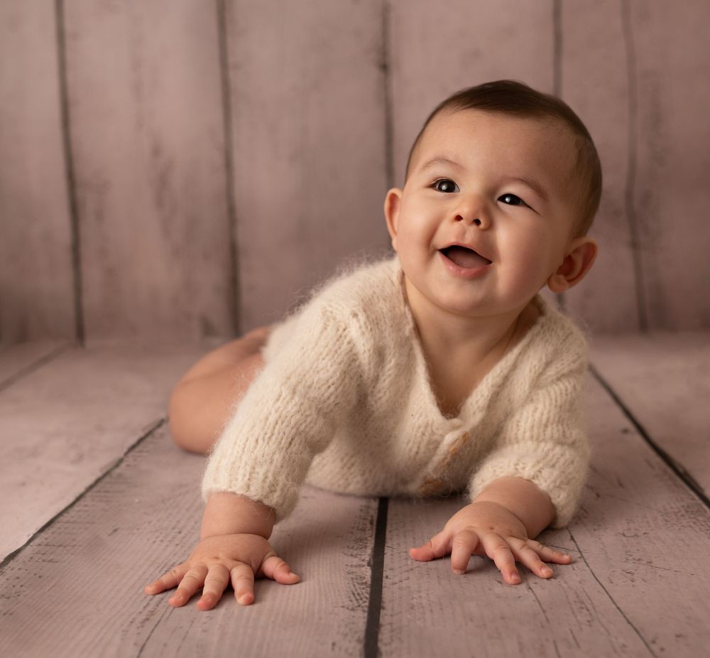 baby boy on stomach smiling in cream outfit photographed by newborn photographer swansea