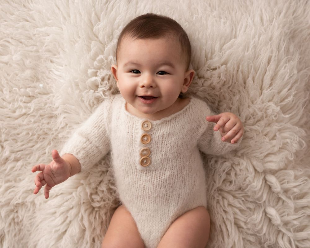 baby boy on cream rug smiling in cream outfit photographed by newborn photographer swansea
