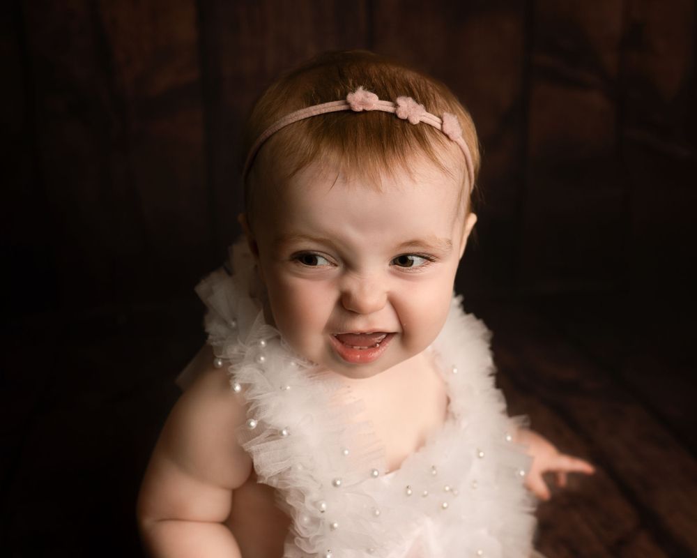 baby girl smiling in white dress on wooden backdrop photographed by newborn photographer swansea