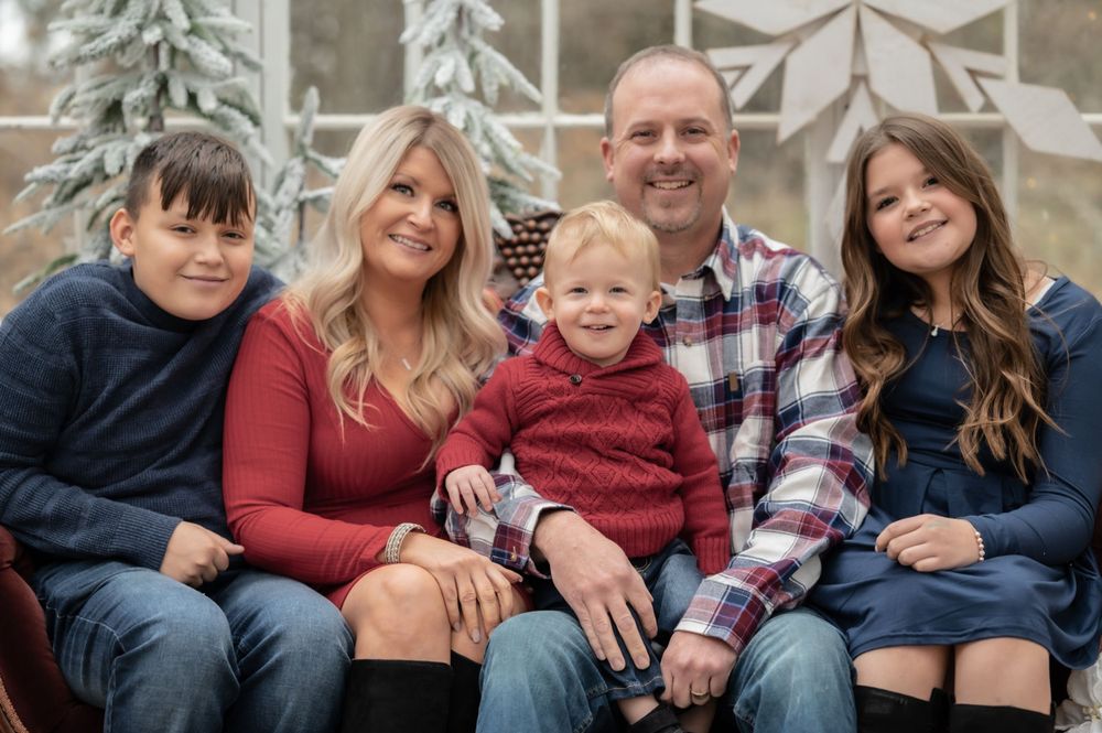 Casual family portrait outdoors with winter scene and decorative snowflakes in background.