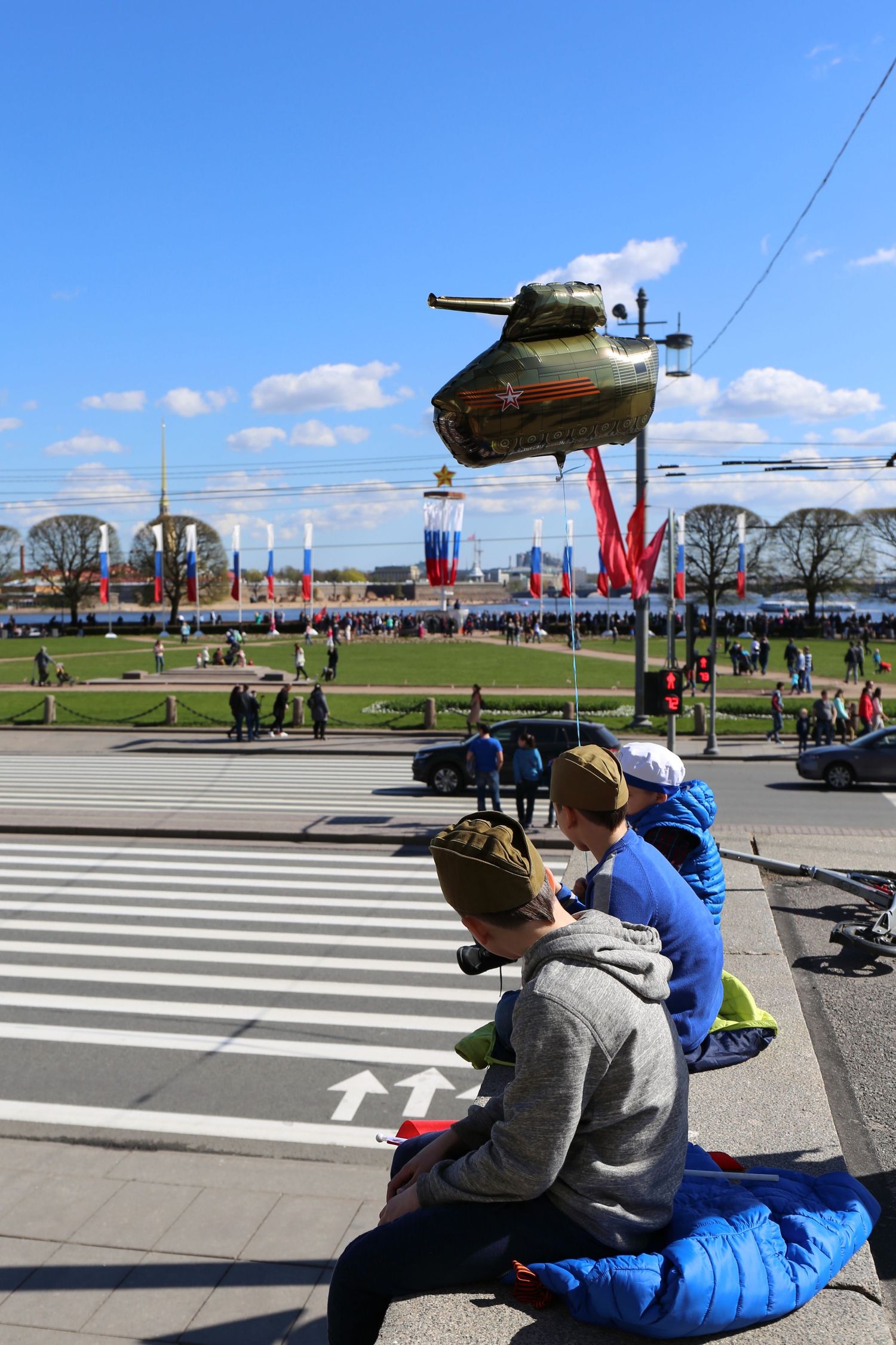 Military tank monument display with photographers capturing it against blue sky.