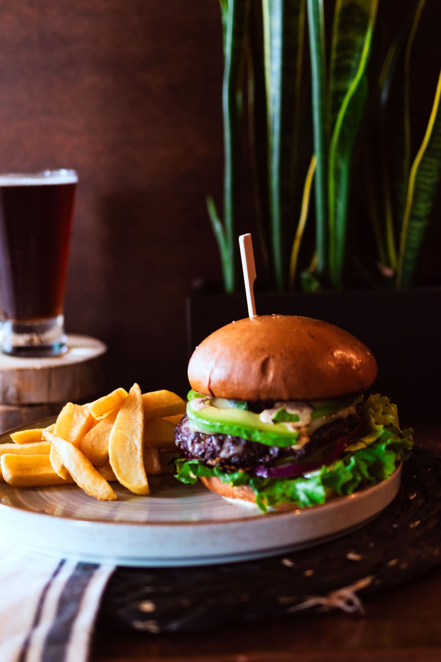 Gourmet burger with fries served on a round plate against a dark background for restaurant branding photography.