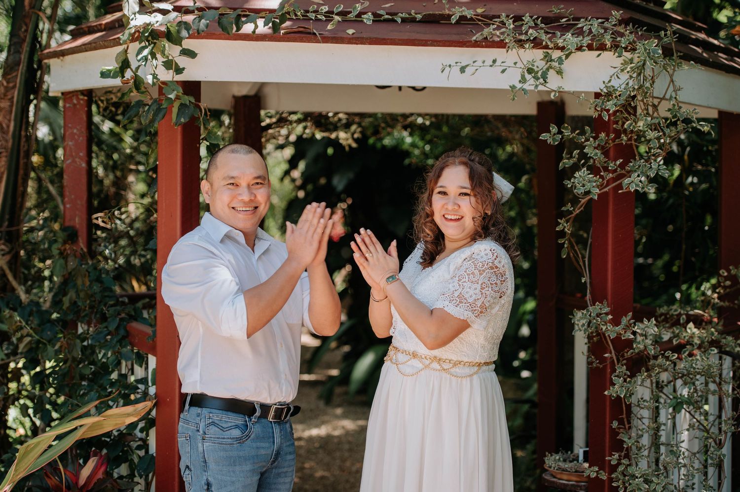 Newlyweds clapping and celebrating during outdoor garden ceremony.