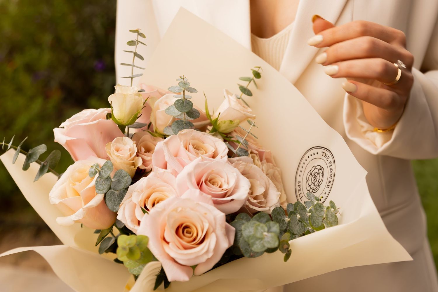 Close-up of delicate pink roses and eucalyptus bouquet wrapped in cream paper held by woman.