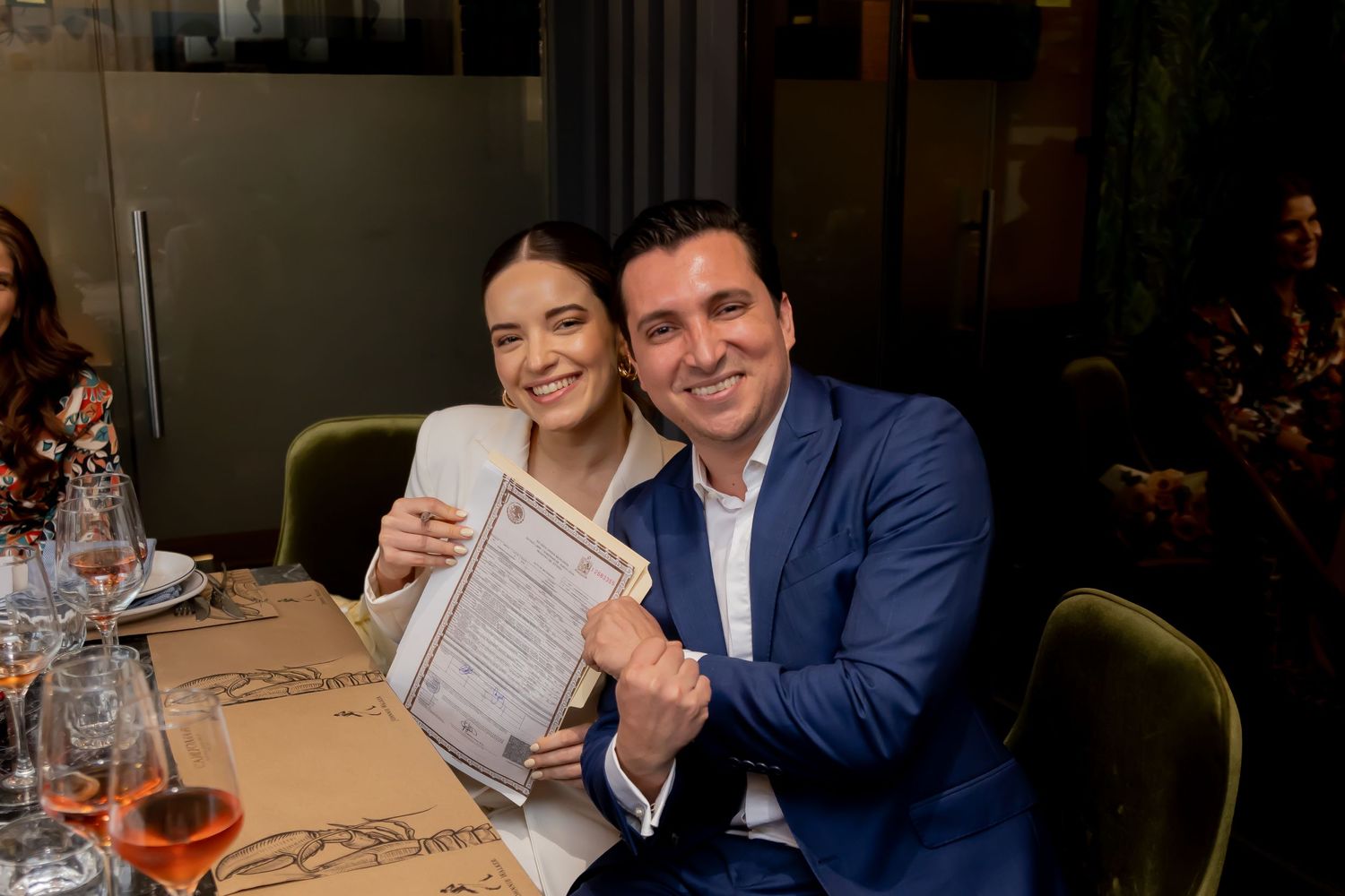 Happy newlyweds smiling and holding their signed wedding certificate at reception dinner.