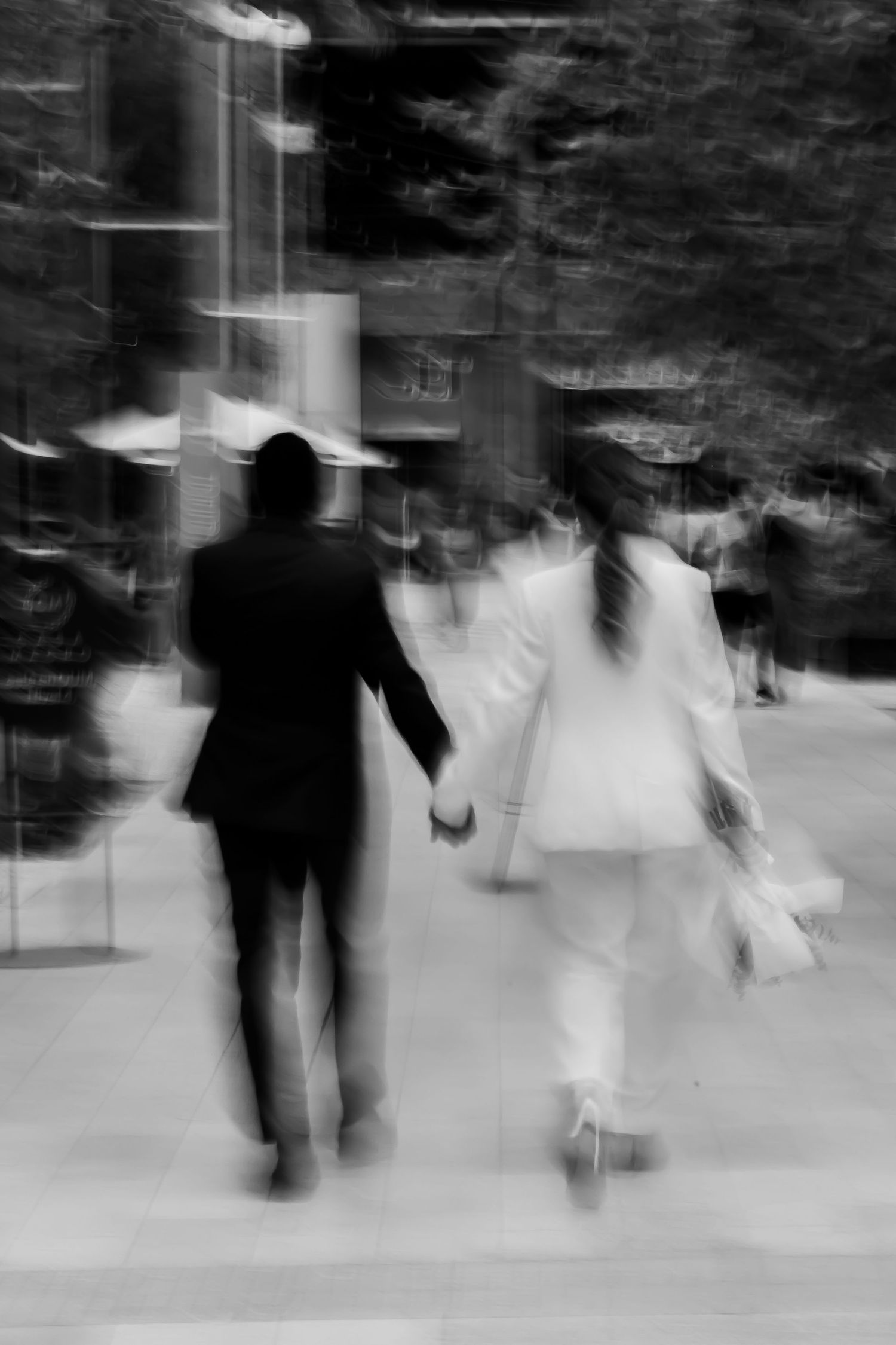 Black and white motion blur photo of newlywed couple holding hands walking together.