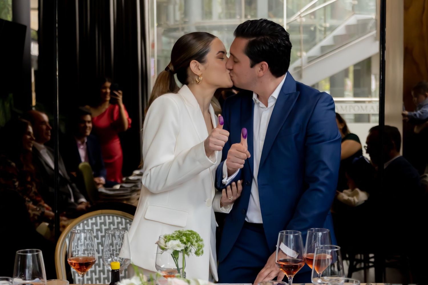 Newlyweds sharing a kiss while holding ink-stained fingers after signing marriage certificate.