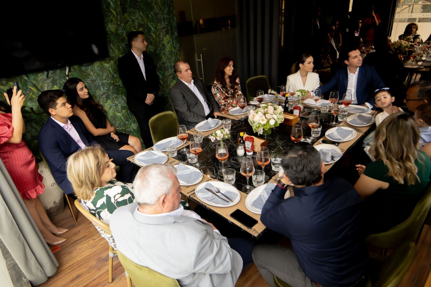 Wedding guests gathered around decorated dining table at elegant indoor reception dinner.