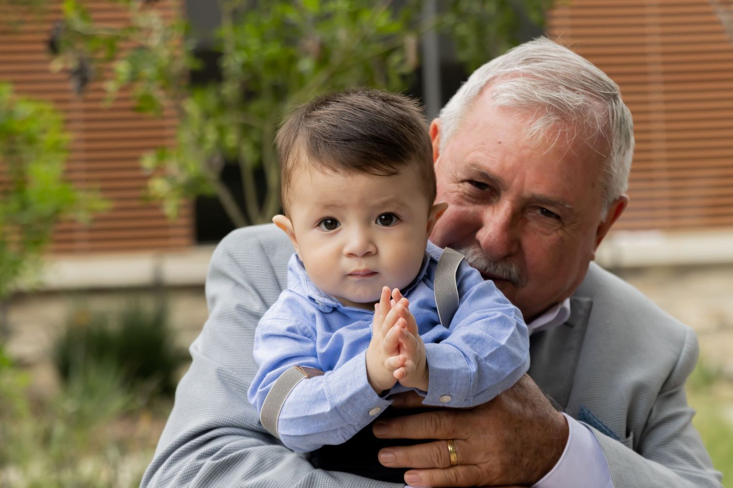 Elderly man with silver hair lovingly holds a happy baby dressed in blue.