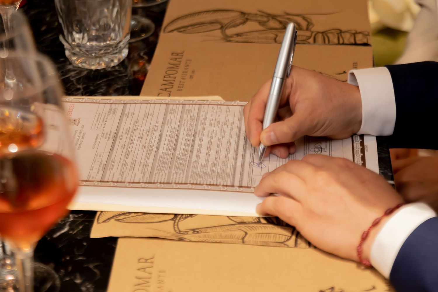 Close-up of groom signing official wedding certificate document at reception dinner table.