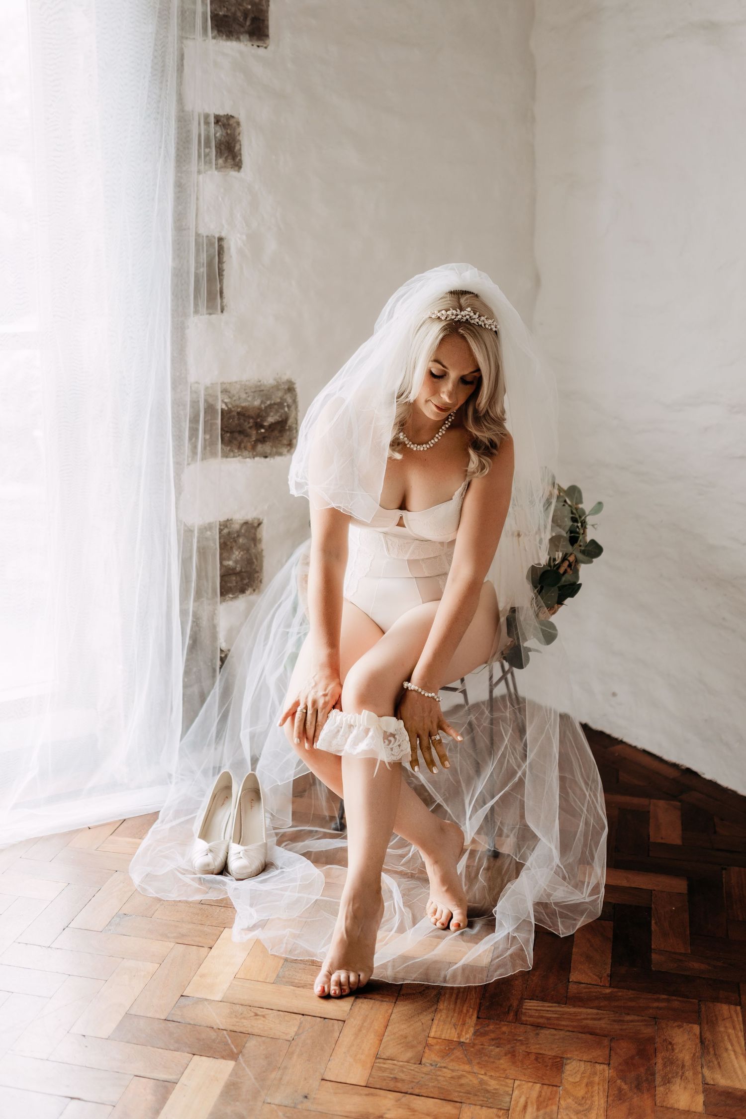 Elegant bridal boudoir scene with wedding shoes and flowing veil on parquet floor.