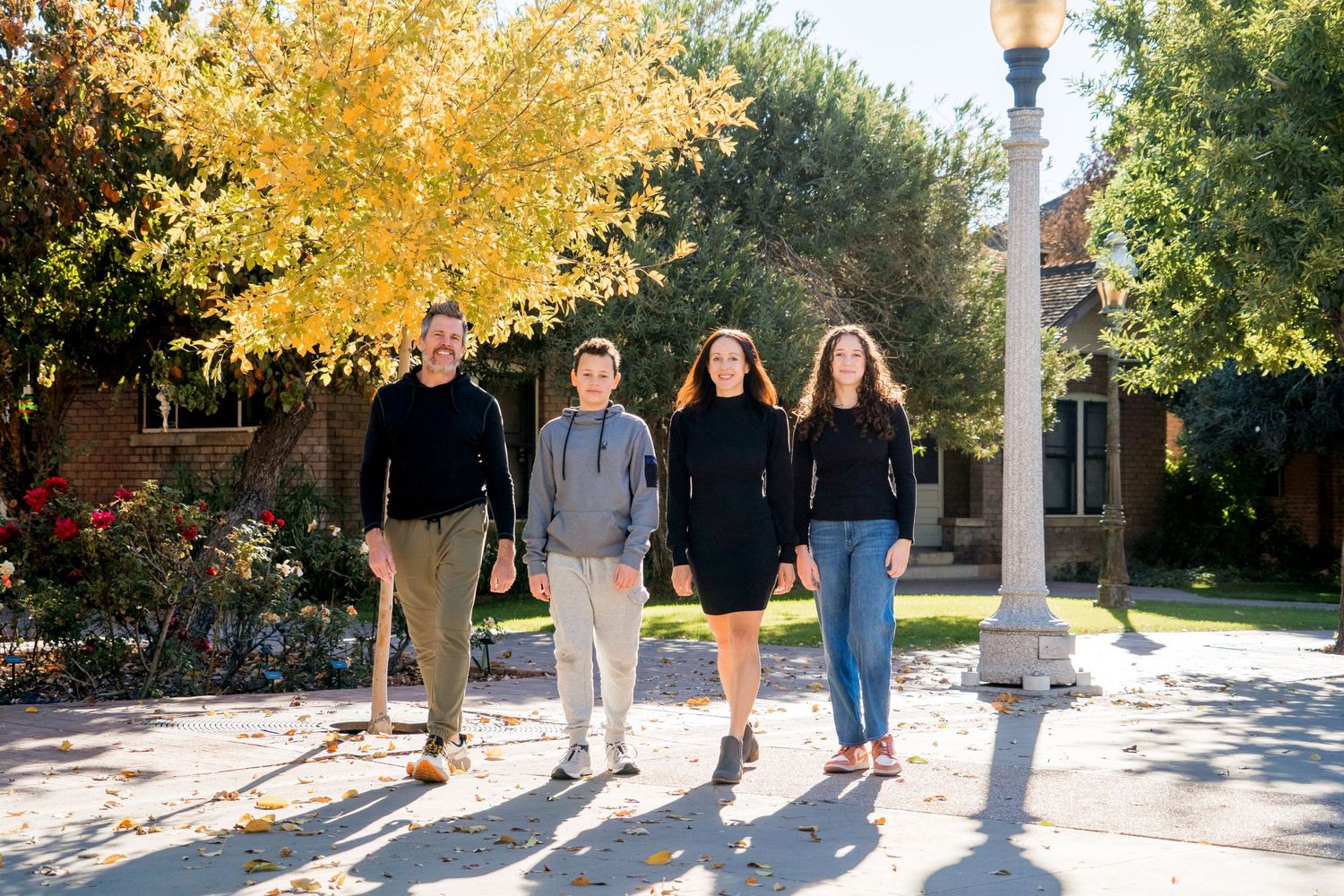 Group walking together on campus sidewalk during fall with golden trees in background.