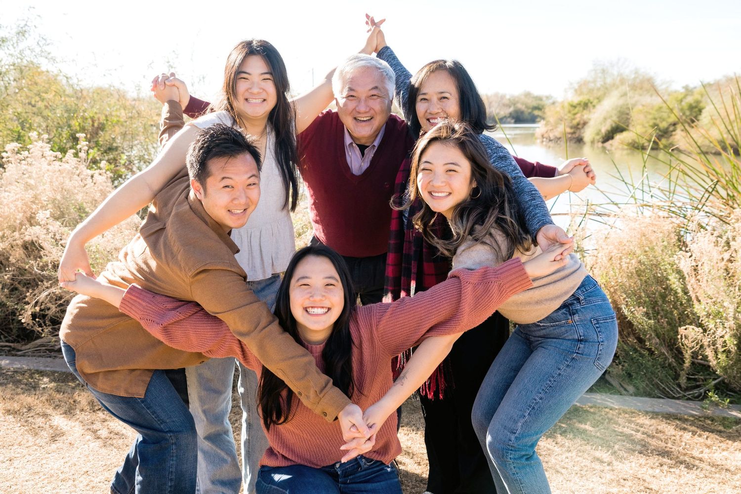 Multi-generational family group poses playfully outdoors near a lake.