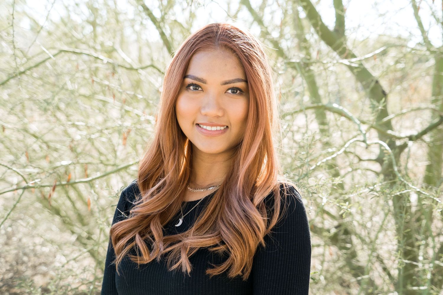 Portrait of woman in black sweater against blurred winter tree background.