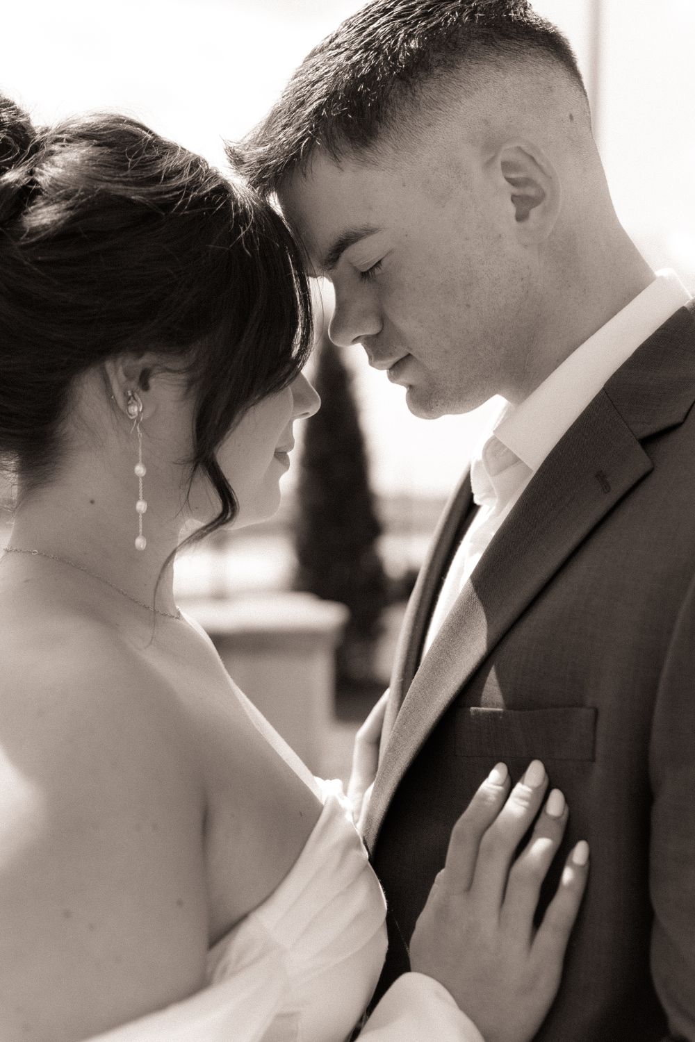 A romantic black and white portrait of a couple in wedding attire sharing an intimate moment with their foreheads touching.